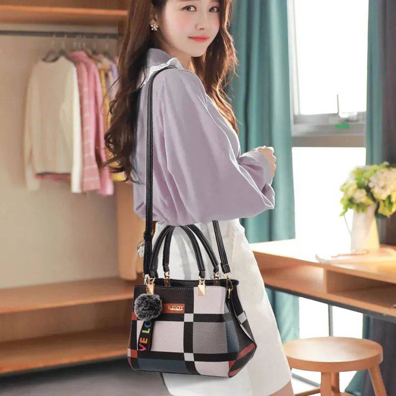 Mulher usando bolsa tote feminina estampada Kouy com padrão xadrez multicolorido e alças pretas, carregada no ombro, em ambiente de casa ou escritório, com chaveiro de pompom.