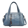Bolsa tote estruturada azul acinzentado com textura de couro e costura decorativa, alças trançadas e chaveiro de borla.