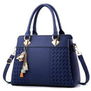 Bolsa tote feminina estruturada de couro azul marinho, com detalhes texturizados em relevo, alça transversal e chaveiro de pássaro dourado com borlas coloridas, em vista frontal.