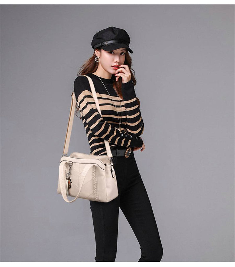 Mulher usando bolsa tote estruturada bege clara com alça transversal, combinando com blusa listrada e calça preta, em estilo casual elegante.