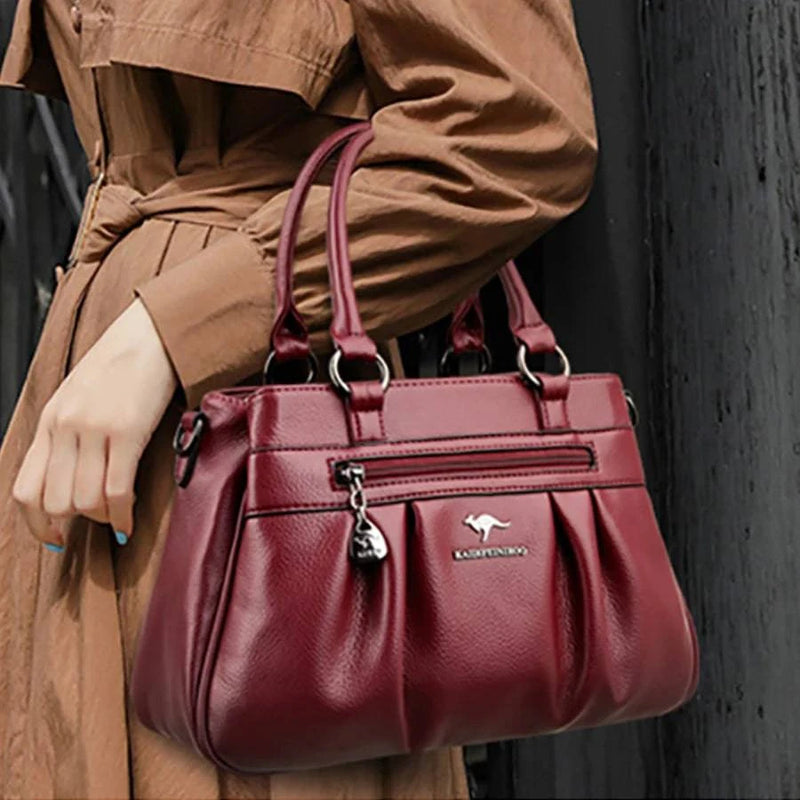 Bolsa Tote Estruturada Feminina Couro Radiance vinho. Alças de mão, zíper frontal com charm, logo metálico. Usada por modelo em trench coat.
