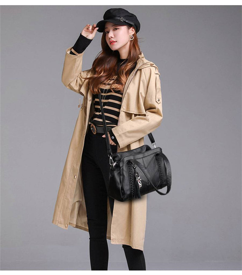 Mulher com bolsa tote preta estruturada com alça de ombro, combinando com trench coat bege, blusa listrada e boina, estilo casual moderno.
