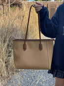 Bolsa tote feminina de couro bege com alças marrom, segurada por mulher em ambiente externo