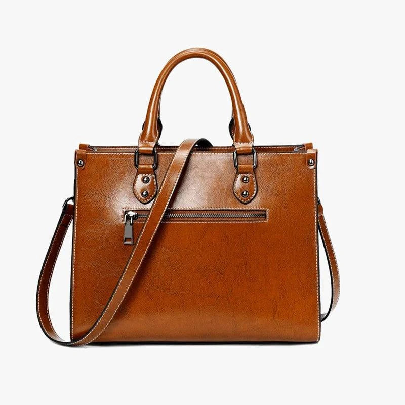 Bolsa Tote Feminina Couro Legítimo Velvet marrom. Parte traseira com bolso de zíper e costura branca. Acabamento brilhante. Praticidade e estilo.