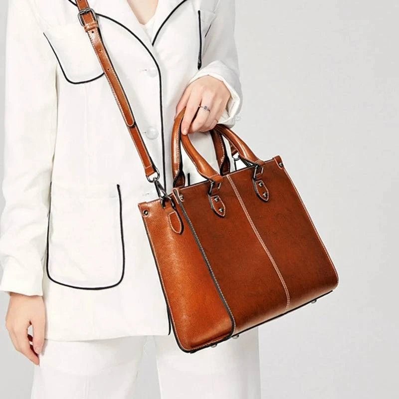 Bolsa Tote Feminina Couro Legítimo Velvet marrom. Acabamento brilhante, costura branca, alças e ferragens metálicas. Usada por modelo. Elegante e estruturada.