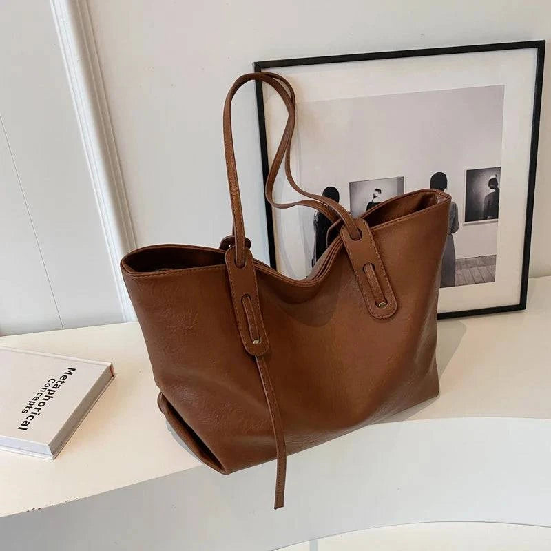 Bolsa Tote Feminina em Couro Marrom com alça longa, vista de frente e lateral, estilo elegante e minimalista.