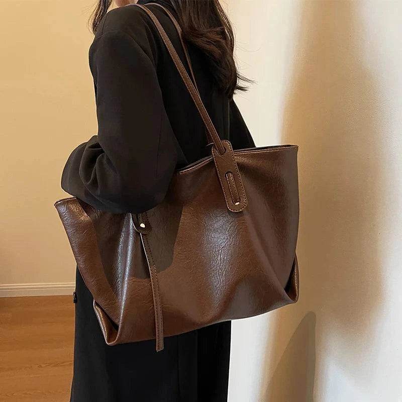 Mulher segurando bolsa tote feminina de couro marrom com acabamento liso e alças duplas
