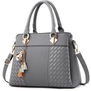 Bolsa tote feminina estruturada de couro cinza, com detalhes texturizados em relevo, alças de mão e alça transversal, adornada com chaveiro de pássaro dourado e borlas coloridas.