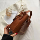 Bolsa tote pequena de couro marrom com bolso frontal tachado e alça estampada