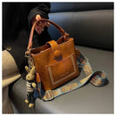Bolsa tote de couro marrom com bolso frontal, alça estampada e charm de coelho