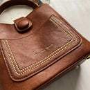 Bolsa transversal de couro marrom com detalhes de tachas douradas e botão decorativo