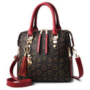 Bolsa tote estruturada preta com monograma dourado, alças vermelhas e alça tiracolo a tiracolo, com chaveiro de gato e borla