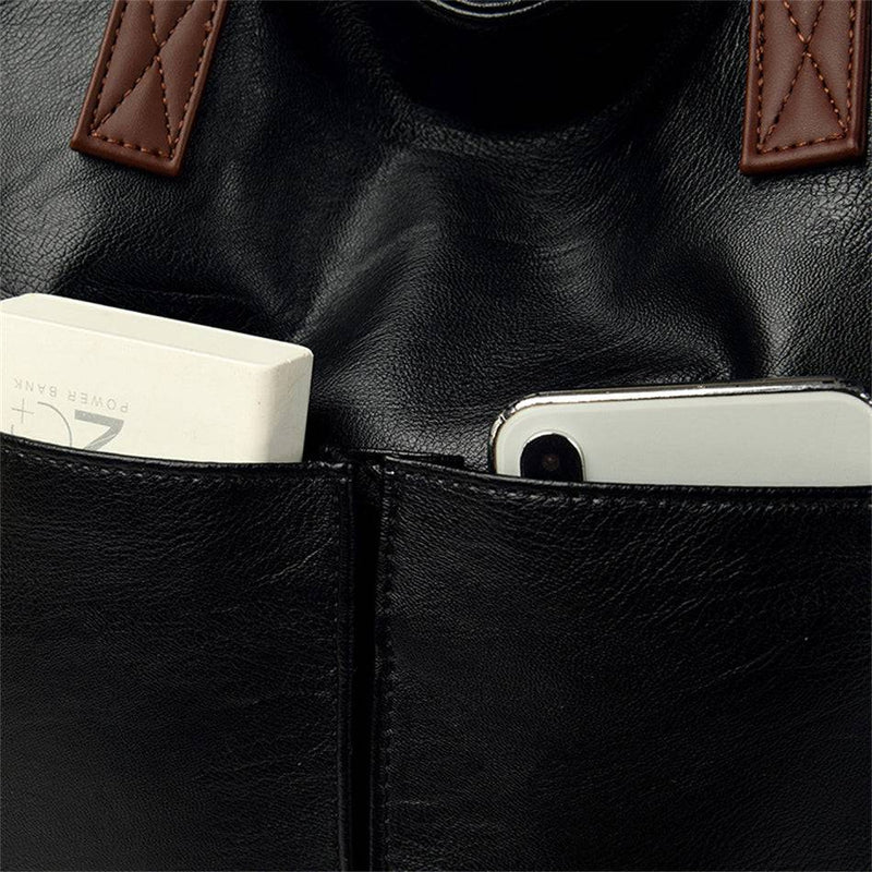 Detalhe dos bolsos frontais da bolsa tote Sofia preta, com power bank e celular visíveis, destacando a textura do couro e a praticidade dos compartimentos externos.