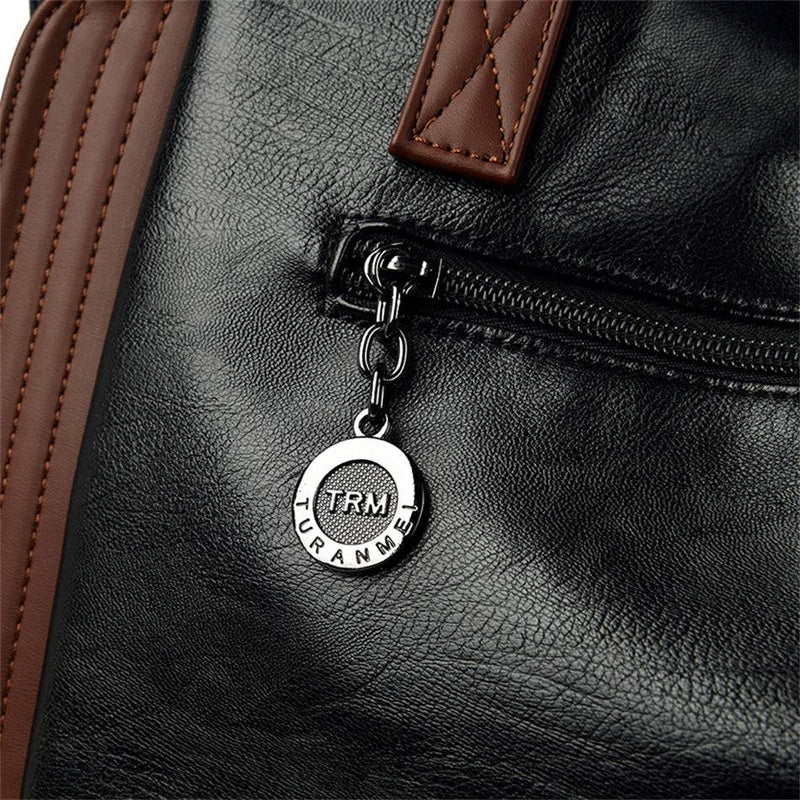Detalhe em close-up do zíper da bolsa tote Sofia preta, destacando o puxador metálico e o chaveiro redondo com a inscrição "TRM", junto ao acabamento marrom.
