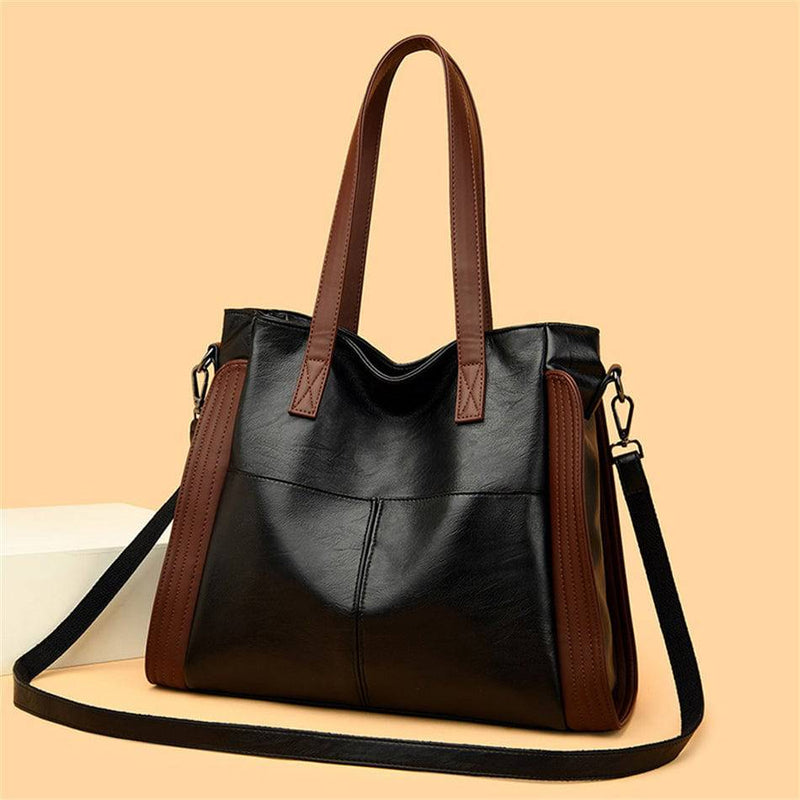 Bolsa tote feminina de couro sintético Sofia preta com detalhes laterais e alças em marrom, apresentando alça transversal estendida e design moderno, em fundo bege.