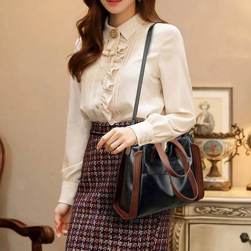 Mulher com blusa de babados e saia xadrez usando bolsa tote feminina Sofia preta com detalhes marrons e alça transversal, ideal para um visual de escritório.