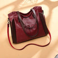 Bolsa tote feminina de couro sintético Sofia em vermelho bordô com detalhes marrons nas laterais e alça transversal, design espaçoso e elegante.