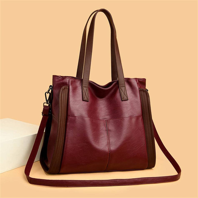 Bolsa tote feminina de couro sintético Sofia cor vinho com painéis laterais e alças marrons, design elegante e alça transversal para uso versátil, em fundo bege.