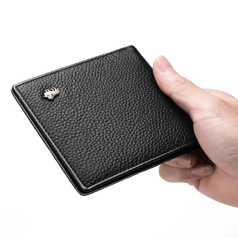 Mão segurando a carteira masculina Bison de couro legítimo preta, exibindo sua textura granulada e o elegante emblema metálico, destacando o caimento e o design compacto.