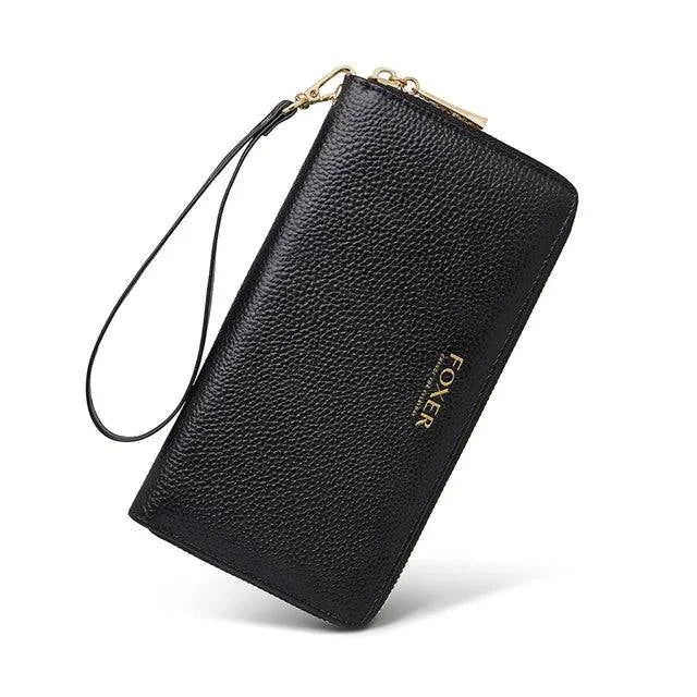 Carteira feminina de couro casual preta com textura granulada, alça de pulso removível e fecho de zíper dourado, exibida em ângulo dinâmico com logotipo FOXER discreto.