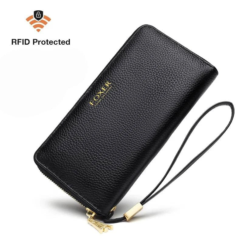 Carteira feminina de couro casual preta com textura granulada, fecho de zíper dourado, alça de pulso removível e indicação de proteção RFID para segurança dos dados.
