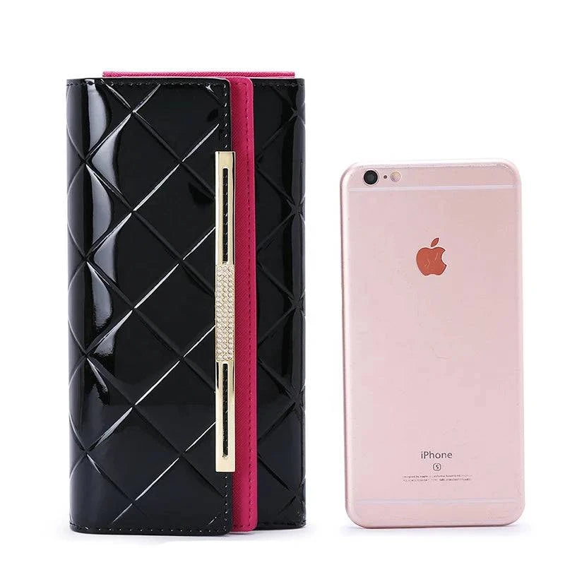 Carteira feminina de couro legítimo preta envernizada com padrão matelassê, detalhe de barra metálica e aba pink, exibindo comparativo de tamanho com um smartphone.