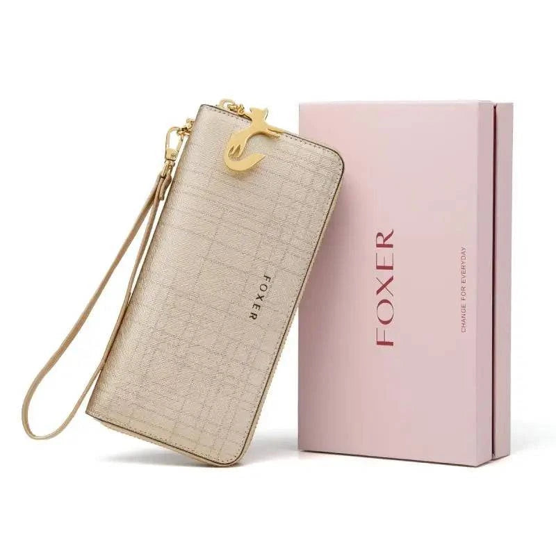 Carteira feminina de couro Mônaco dourada/champanhe com textura sutil e charm de gato dourado, apresentada inclinada ao lado de sua caixa de presente FOXER, ideal para presentear com estilo.