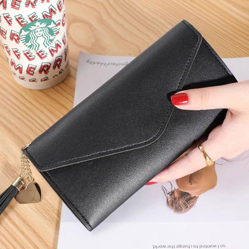 Mão feminina com unhas vermelhas segurando carteira de couro multifuncional preta com fecho de aba e borla, sobre um documento, com copo de café descartável ao fundo, em cena casual.