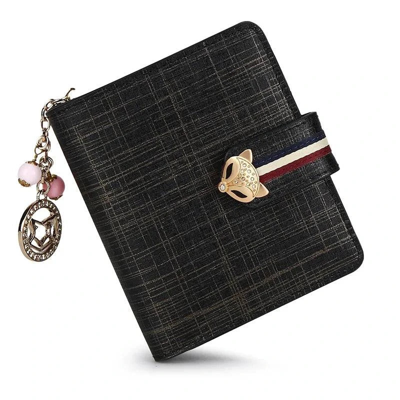 Carteira feminina pequena elegante preta com textura sutil quadriculada, fecho de raposa dourado e aba com tira listrada, adornada com charm de bolinhas e pendente dourado.