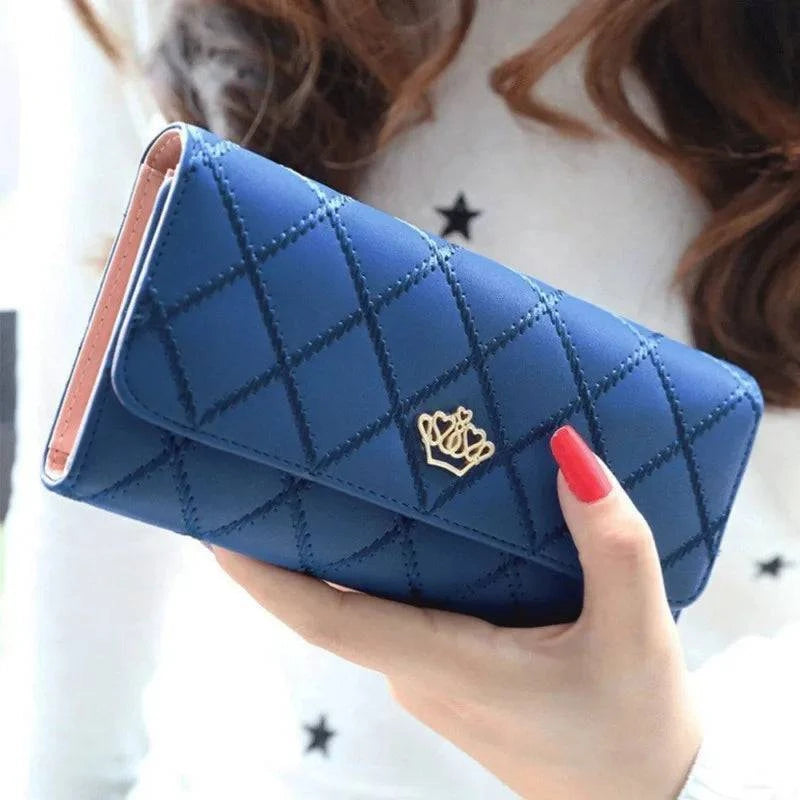 Mão feminina com unhas vermelhas segurando carteira feminina de couro sofisticada azul, acolchoada em matelassê com fecho de coroa dourada, destacando seu design elegante.