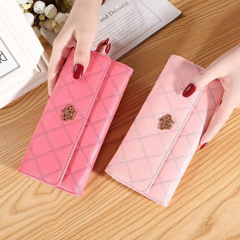 Duas carteiras femininas de couro sofisticadas, uma rosa escuro e outra rosa claro, ambas acolchoadas em matelassê com fecho de coroa dourada, exibidas por mãos em superfície de madeira.