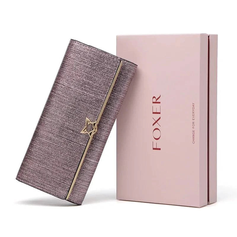 Carteira feminina de couro luxuosa rosa metálico com acabamento brilhante e fecho de estrela dourado, apresentada ao lado de sua caixa de presente da marca FOXER, em vista frontal para e-commerce.