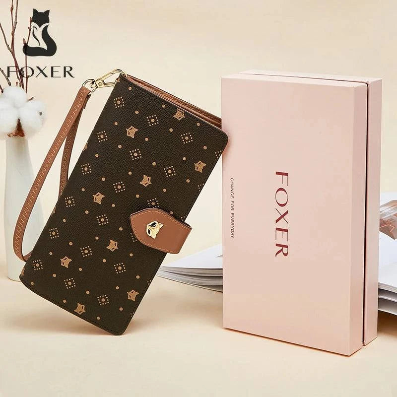 Carteira feminina de mão slim marrom com estampa de logotipo dourado e aba com fecho de raposa, exibida ao lado de sua caixa de presente rosa da marca "FOXER", ideal para presente.