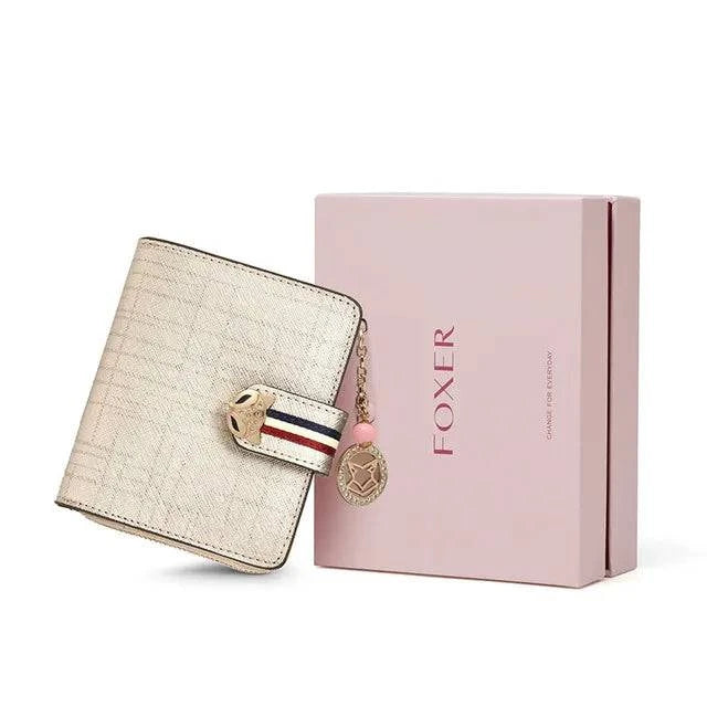 Carteira feminina pequena elegante dourada/champanhe metálica com textura brilhante e fecho de raposa, exibida ao lado de sua caixa de presente rosa da marca "FOXER", ideal para presente.
