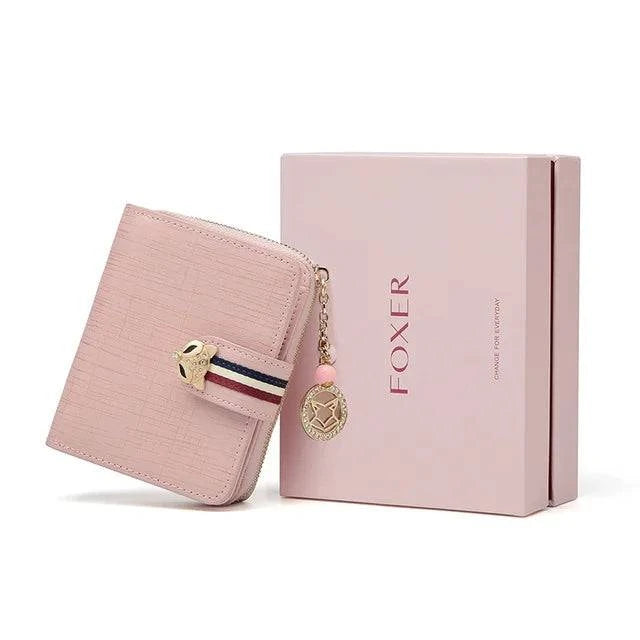Carteira feminina pequena elegante rosa claro com fecho de raposa e tira listrada, exibida inclinada ao lado de sua caixa de presente rosa da marca "FOXER", ideal para presente.