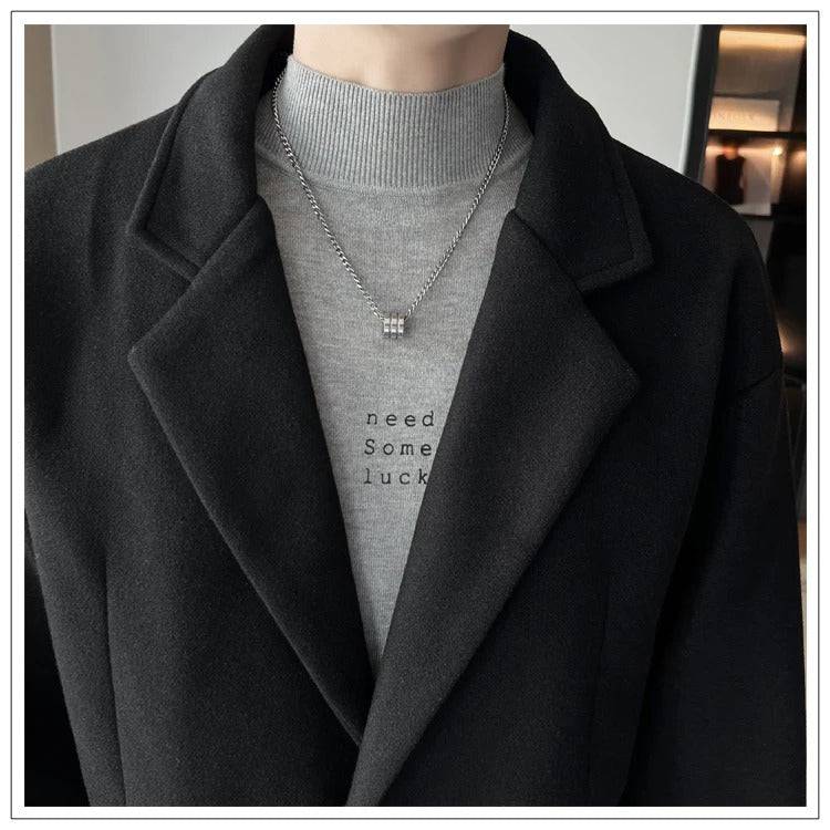 Detalhe do sobretudo masculino de lã preto com gola lapela e suéter cinza por baixo. Estilo refinado e contemporâneo.