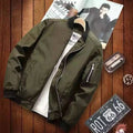Jaqueta bomber masculina verde militar aberta sobre camiseta branca, em ambiente rústico com placa 'Route 66' e revista. Estilo aventureiro.