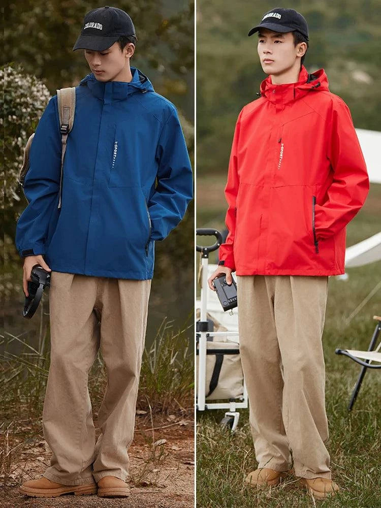 Duas fotos de um modelo masculino asiático em ambiente externo com jaquetas corta-vento com capuz embutido: uma azul, segurando fones de ouvido e mochila, e outra vermelha, segurando uma câmera. Ambas combinadas com boné preto e calças cáqui. Versatilidade e estilo para explorar a natureza.