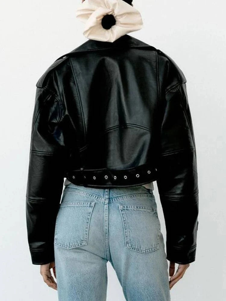 Mulher de costas usando jaqueta de couro feminina Belt preta com cinto e ilhoses, combinada com jeans de lavagem clara e scrunchie no cabelo, evidenciando o luxo moderno e o estilo exclusivo da peça em Embu das Artes.