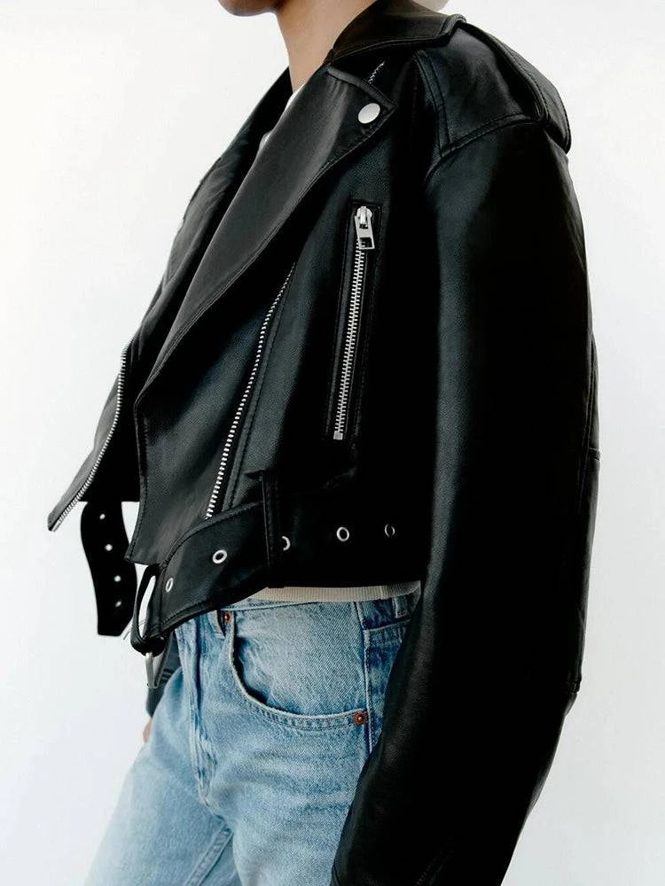 Perfil de mulher usando jaqueta de couro feminina Belt preta, estilo biker com zíperes prateados, lapelas e cinto pendente, combinada com jeans, realçando o luxo e a atitude do design exclusivo em Embu das Artes.