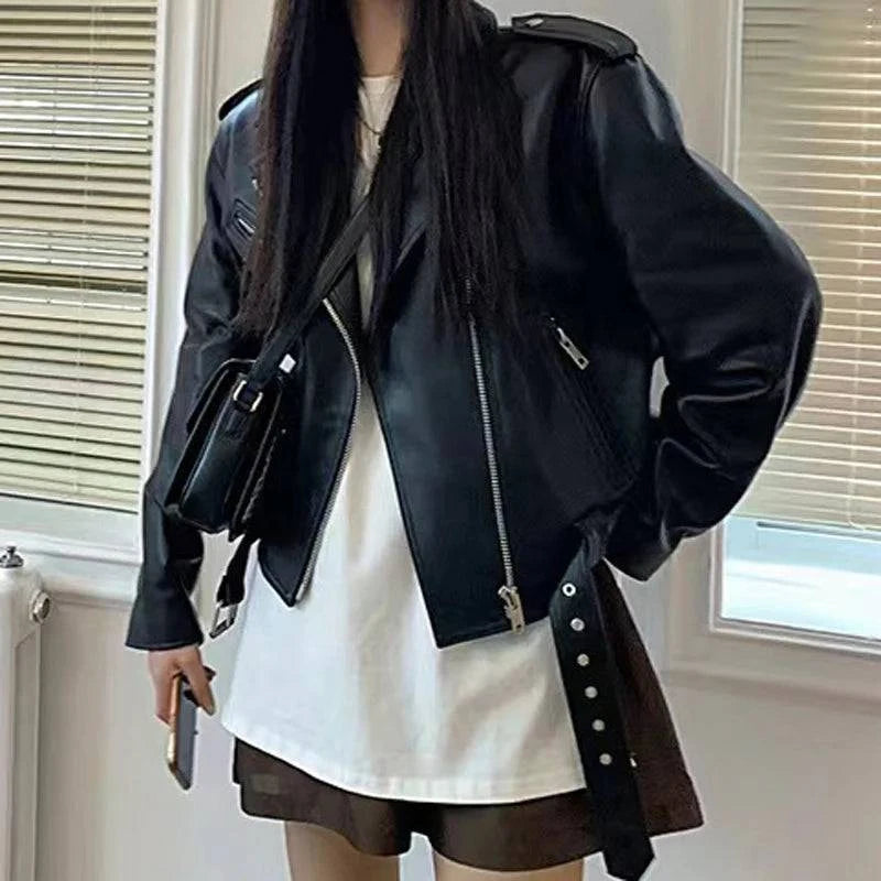 Mulher vestindo jaqueta de couro feminina preta, estilo biker com zíperes e cinto, combinada com camiseta branca e shorts, exibindo um visual urbano de luxo e atitude atemporal.