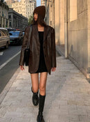 Mulher em jaqueta de couro oversized marrom com vestido preto e botas altas em rua urbana