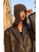Mulher em jaqueta de couro oversized marrom e beanie, ajustando a aba do gorro