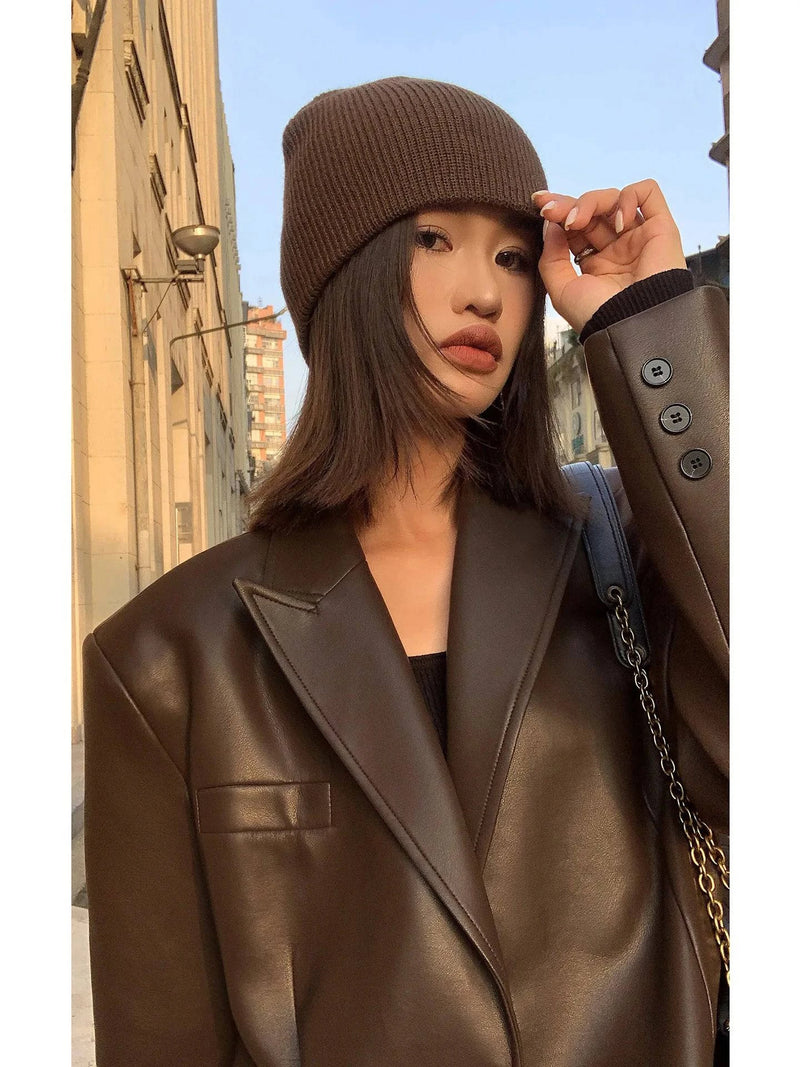 Mulher caminhando na rua em Embu das Artes, usando jaqueta de couro oversized feminina marrom sobre vestido preto curto, com botas altas e beanie, exibindo um visual de luxo moderno e exclusivo para o inverno.
