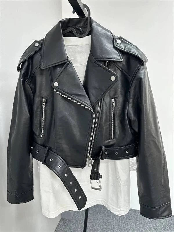 Jaqueta de couro feminina preta, estilo biker com cinto ajustável, lapelas largas, zíperes prateados e botões de pressão, transmitindo um visual de luxo e atitude.