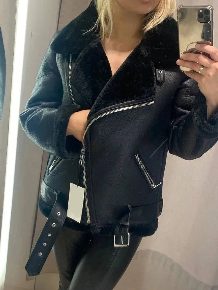 Mulher vestindo jaqueta de couro Rockstar preta com forro de pele sintética exposto, zíper assimétrico e cinto com fivela, evidenciando o design exclusivo e o calor luxuoso da peça.