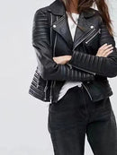Mulher com jaqueta de couro preta estilo moto, ombros e mangas acolchoados, zíperes metálicos.