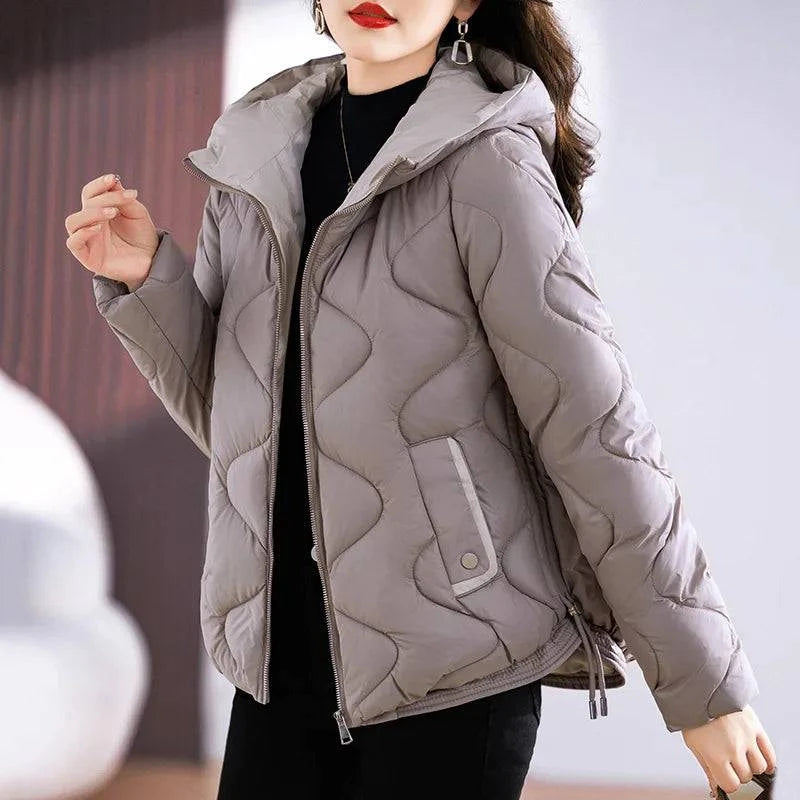 Jaqueta puffer feminina em tom cinza-taupe sofisticado, com capuz e acolchoamento ondulado único, destacando os detalhes refinados e o caimento elegante para um visual de distinção.