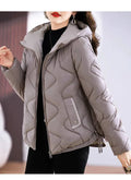 Jaqueta puffer feminina em tom cinza-claro sofisticado, com capuz e acolchoamento ondulado, destacando detalhes de bolso e ajuste na barra, ideal para um inverno luxuoso e prático.