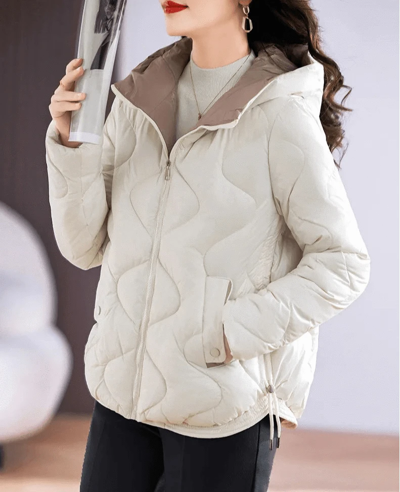 Jaqueta puffer feminina em tom cinza-claro, com acolchoamento em padrão de ondas e capuz forrado, exibindo detalhes de bolso e ajuste, oferecendo elegância e calor exclusivo para o inverno.